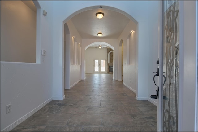 hallway with baseboards, stone finish floors, and arched walkways