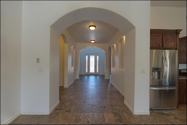 hallway with baseboards, arched walkways, and stone tile flooring