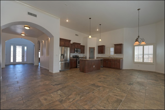 kitchen featuring appliances with stainless steel finishes, open floor plan, baseboards, a towering ceiling, and a center island