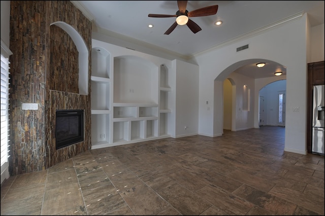 unfurnished living room with built in shelves, ceiling fan, a tile fireplace, ornamental molding, and baseboards