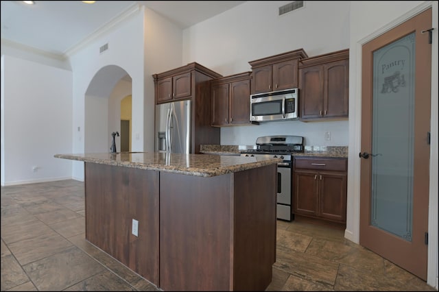 kitchen with appliances with stainless steel finishes, dark stone counters, crown molding, a kitchen island, and arched walkways