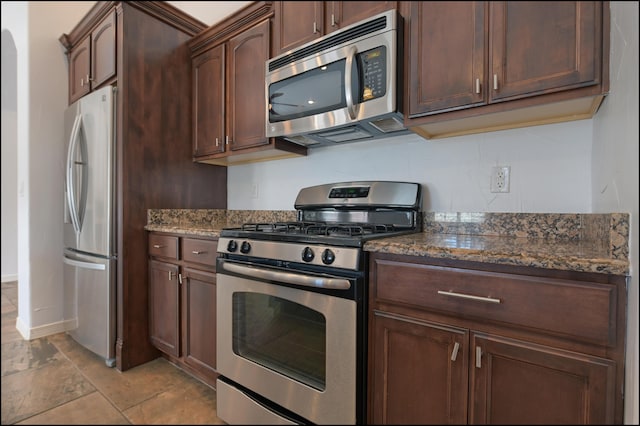 kitchen featuring appliances with stainless steel finishes, dark stone counters, and dark brown cabinetry