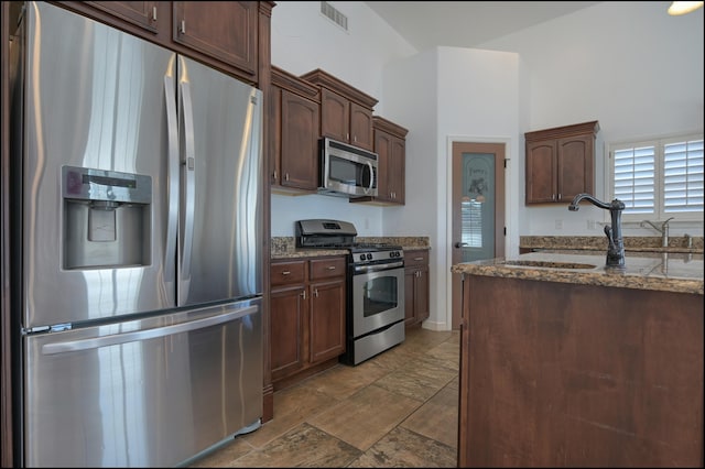 kitchen featuring stainless steel appliances, a sink, dark stone countertops, and dark brown cabinetry