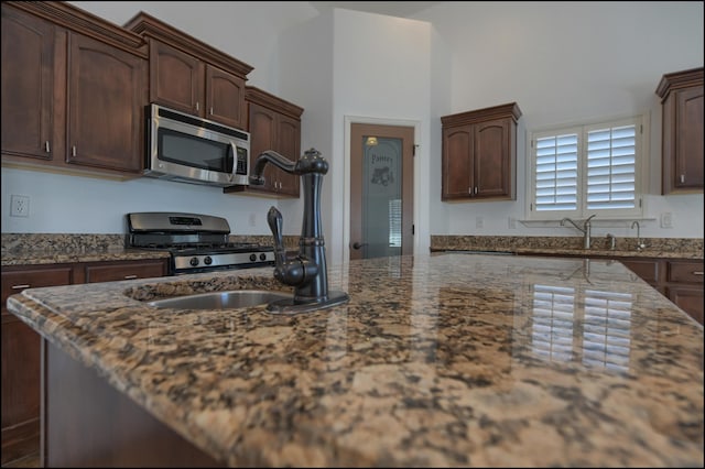 kitchen with stainless steel microwave, gas range oven, dark stone countertops, and dark brown cabinetry