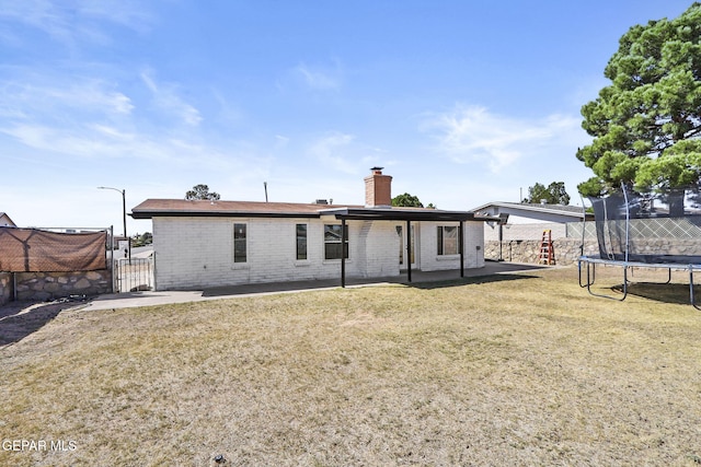back of property featuring a trampoline, a chimney, brick siding, a patio, and a gate