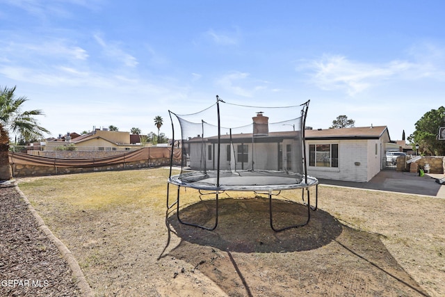 rear view of property with a trampoline, brick siding, a chimney, and a patio area