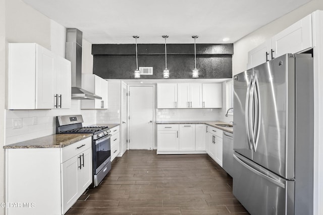 kitchen with appliances with stainless steel finishes, a sink, wall chimney range hood, backsplash, and white cabinets