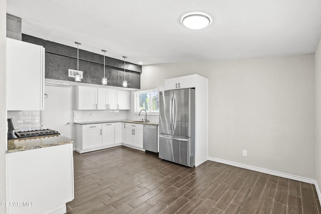 kitchen with appliances with stainless steel finishes, a sink, light stone countertops, tasteful backsplash, and white cabinetry