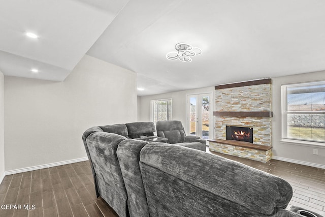 living room with baseboards, wood tiled floors, and a stone fireplace