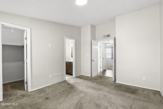 unfurnished bedroom with a spacious closet, carpet floors, ensuite bathroom, a closet, and a textured ceiling
