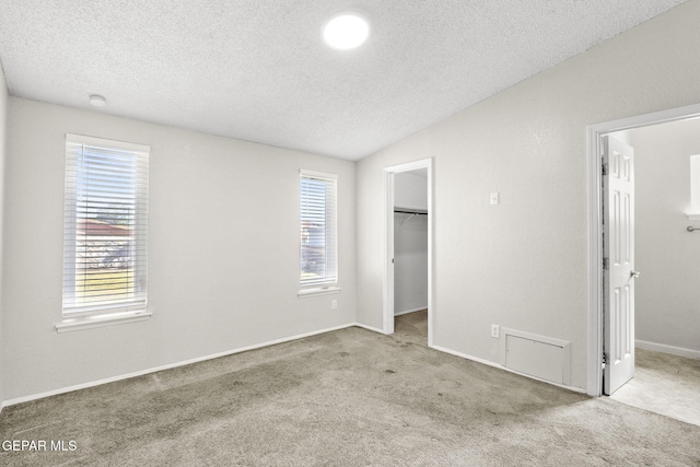 unfurnished bedroom featuring a spacious closet, a textured ceiling, multiple windows, carpet floors, and a closet