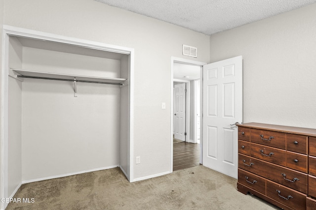 unfurnished bedroom with light colored carpet, a closet, a textured ceiling, and baseboards
