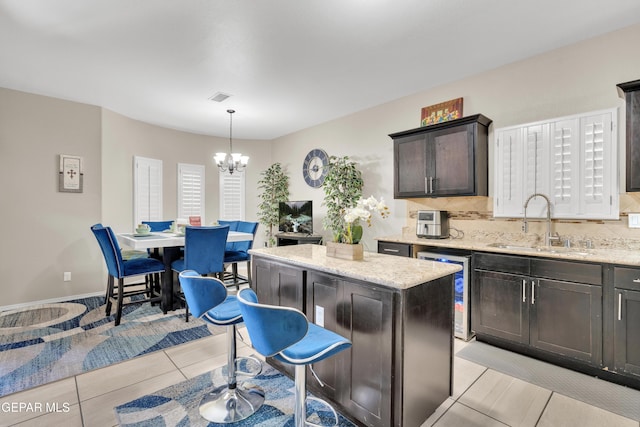kitchen featuring a chandelier, a sink, a kitchen island, light stone counters, and beverage cooler