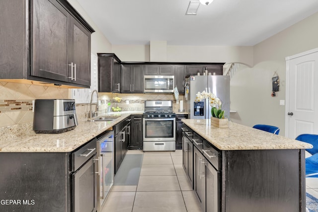kitchen featuring appliances with stainless steel finishes, a sink, light tile patterned flooring, and a center island