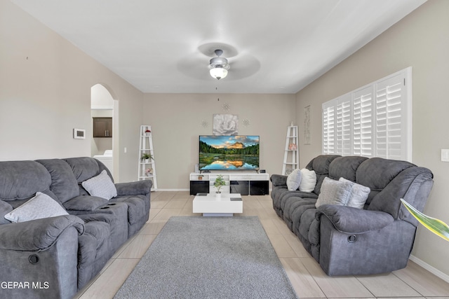 living room featuring arched walkways, a ceiling fan, light tile patterned flooring, and baseboards