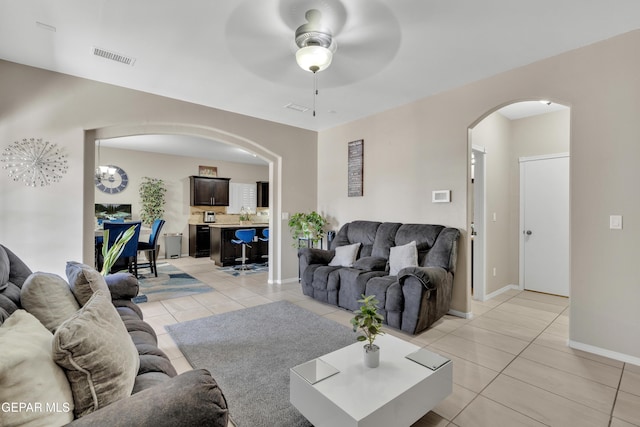 living area featuring arched walkways, light tile patterned floors, a ceiling fan, baseboards, and a chandelier