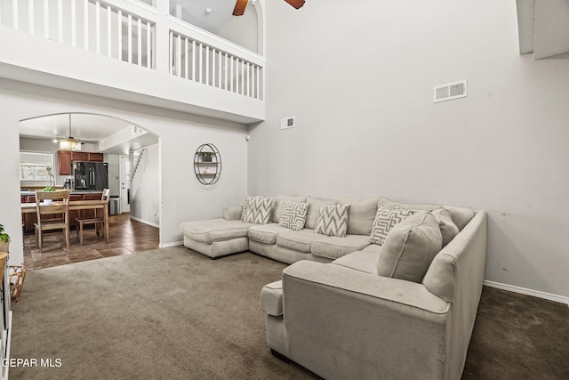 living room featuring arched walkways, a ceiling fan, dark carpet, baseboards, and a high ceiling