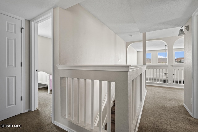 hall with carpet flooring, a textured ceiling, and baseboards