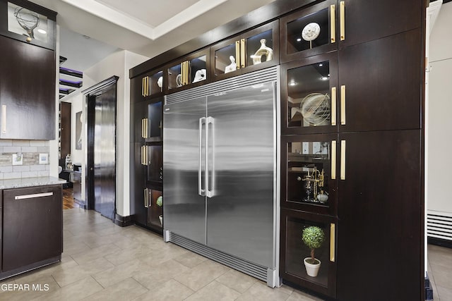 5905 Ojo De Agua Dr, El Paso, TX 79912 - kitchen with built in fridge, dark brown cabinetry, light tile patterned flooring, backsplash, and glass insert cabinets