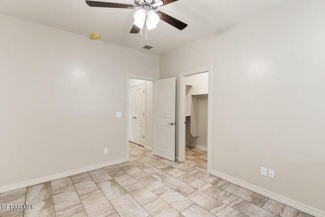 unfurnished bedroom featuring a walk in closet, a ceiling fan, a closet, and baseboards