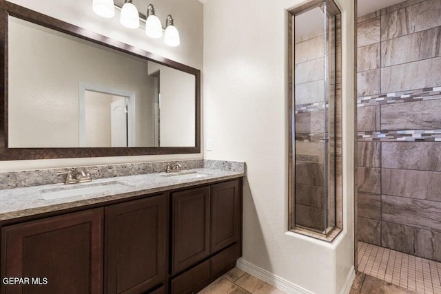 full bathroom with a tile shower, double vanity, and baseboards