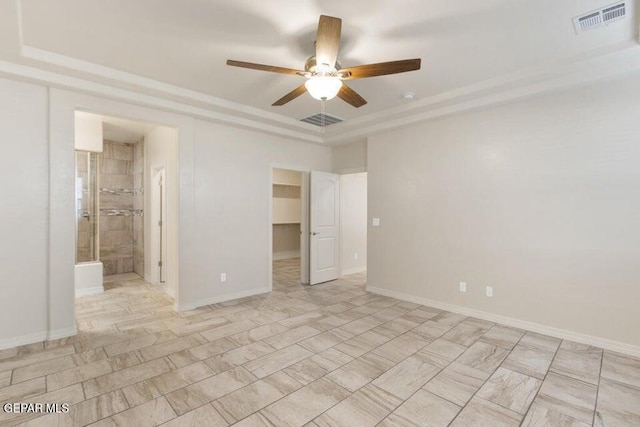 unfurnished bedroom with a walk in closet, a tray ceiling, a closet, and a ceiling fan