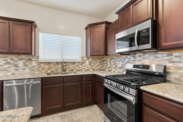 kitchen featuring stainless steel appliances, a sink, tasteful backsplash, light stone countertops, and dark brown cabinetry
