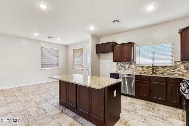 kitchen featuring stainless steel appliances, a sink, decorative backsplash, a center island, and light stone counters