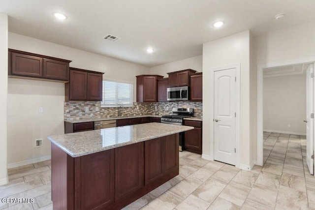 kitchen featuring appliances with stainless steel finishes, tasteful backsplash, a kitchen island, light stone countertops, and dark brown cabinetry