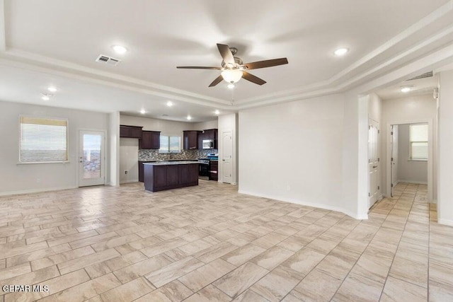 unfurnished living room featuring a tray ceiling, ceiling fan, baseboards, recessed lighting, and crown molding
