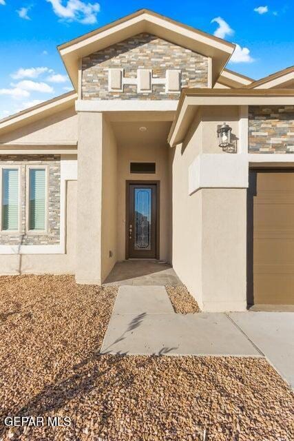 doorway to property featuring stucco siding, an attached garage, driveway, and stone siding