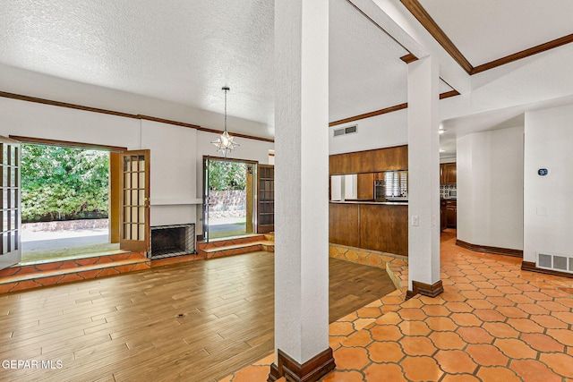 unfurnished living room featuring crown molding, a textured ceiling, baseboards, wood finished floors, and a chandelier