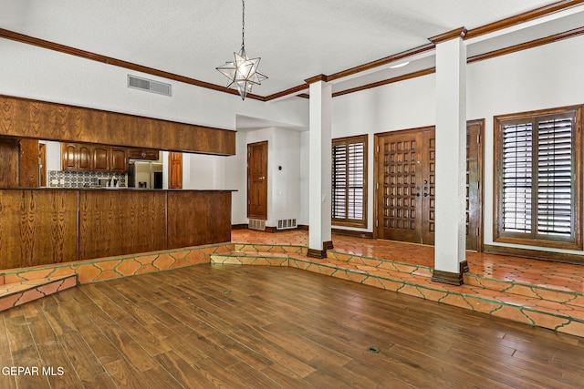 unfurnished living room featuring crown molding, wood finished floors, a textured ceiling, and decorative columns