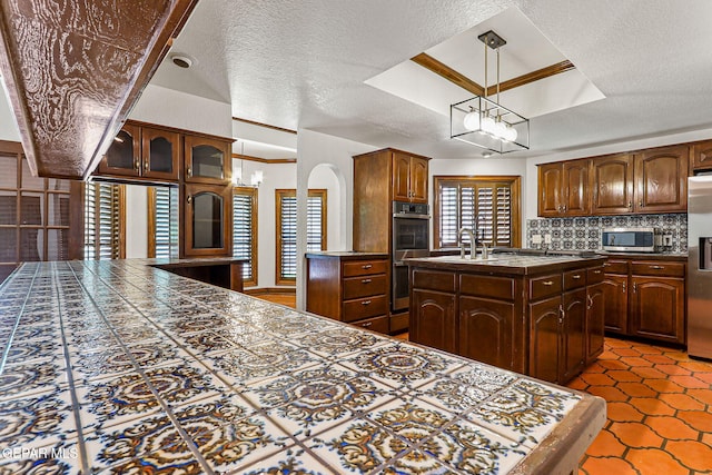 kitchen featuring stainless steel appliances, an island with sink, backsplash, a sink, and dark tile patterned flooring