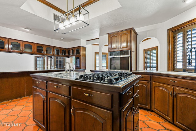 kitchen featuring appliances with stainless steel finishes, a sink, a chandelier, a kitchen island with sink, and arched walkways