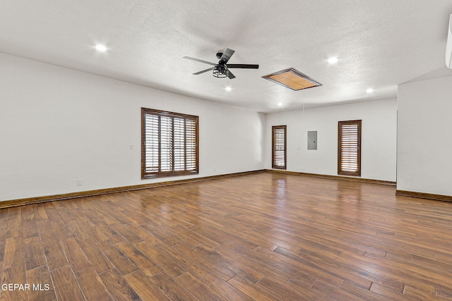 spare room with plenty of natural light, ceiling fan, electric panel, wood finished floors, and a textured ceiling