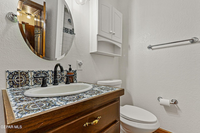 bathroom featuring toilet, vanity, and a textured wall