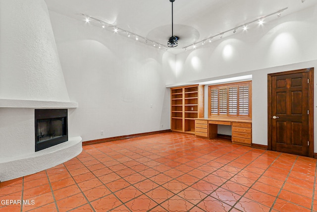 unfurnished living room featuring a towering ceiling, light tile patterned floors, a fireplace, and baseboards