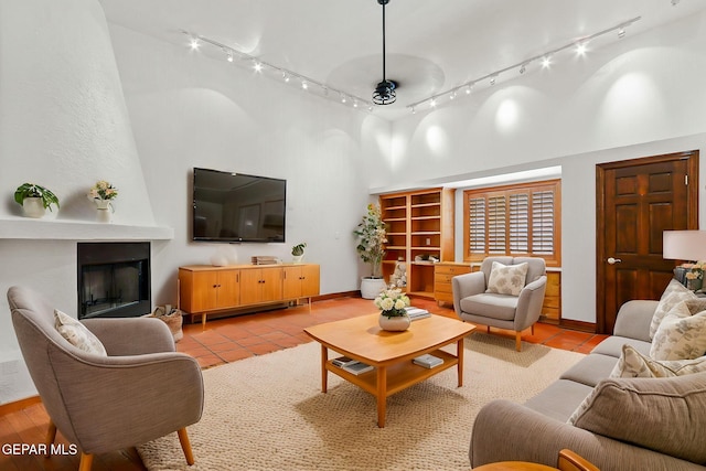 living area with a towering ceiling, rail lighting, light tile patterned floors, and baseboards