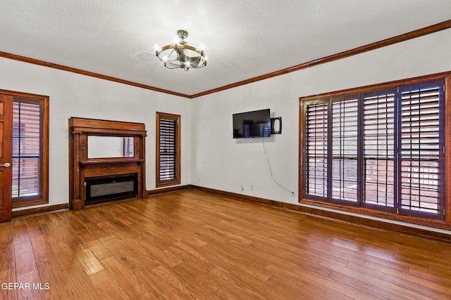 unfurnished living room featuring a chandelier, crown molding, hardwood / wood-style flooring, a glass covered fireplace, and baseboards