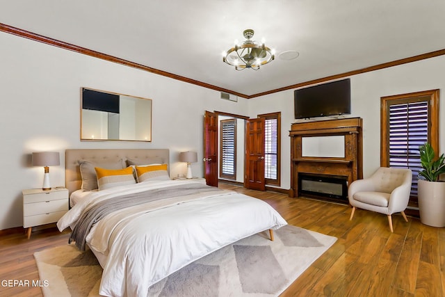 bedroom featuring a chandelier, ornamental molding, wood finished floors, baseboards, and a glass covered fireplace