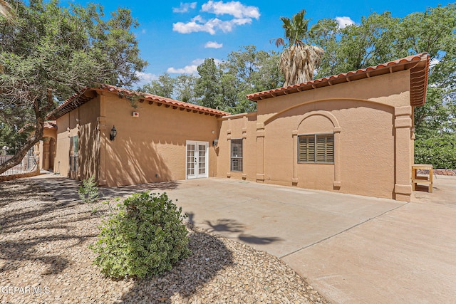 back of property featuring a tile roof, french doors, stucco siding, and a patio