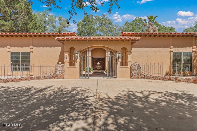 mediterranean / spanish home with fence, stucco siding, and a tiled roof