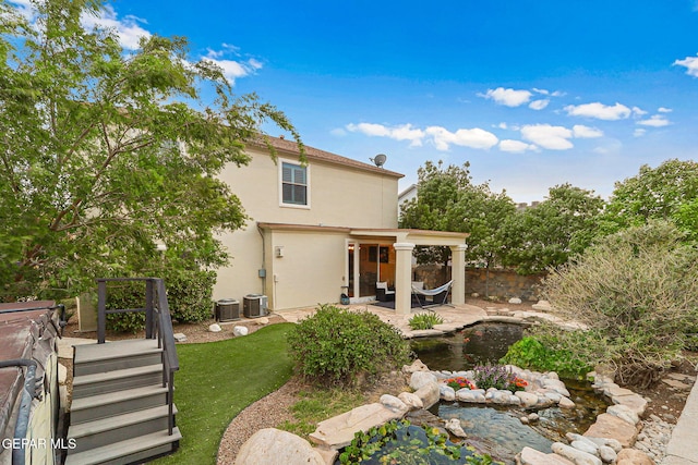 rear view of property with stucco siding, a patio area, fence, central AC, and a small pond