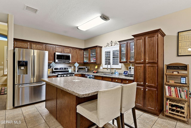 kitchen with appliances with stainless steel finishes, a sink, light tile patterned floors, glass insert cabinets, and a textured ceiling