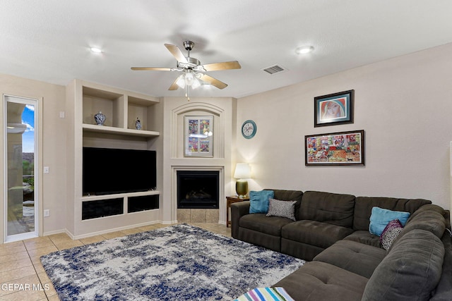 living area with light tile patterned flooring, built in features, ceiling fan, baseboards, and a fireplace