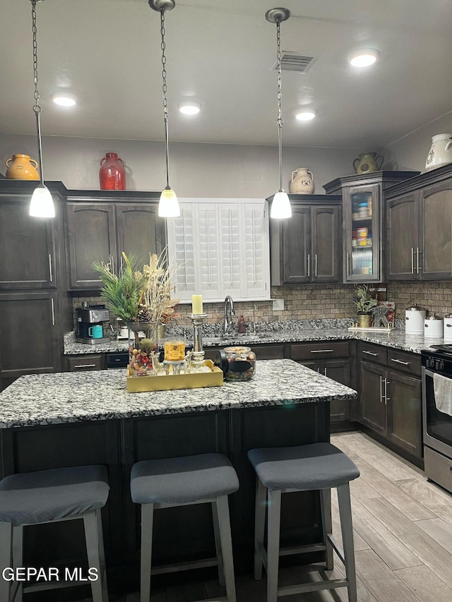 14233 Richard Wiles Ave, El Paso, TX 79938 - kitchen with stainless steel range with gas cooktop, a breakfast bar, decorative backsplash, a kitchen island, and light stone countertops