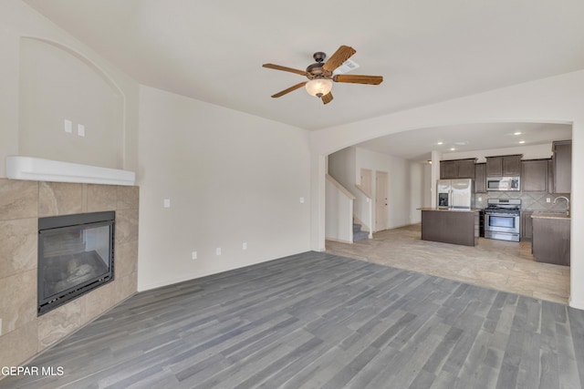 13824 Hollywood Dr, Horizon City, TX 79928 - unfurnished living room featuring light wood finished floors, a fireplace, arched walkways, and a ceiling fan