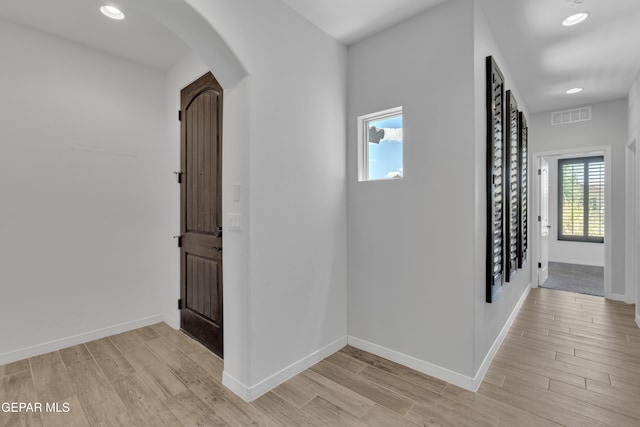 hall featuring arched walkways, light wood-style floors, baseboards, and recessed lighting