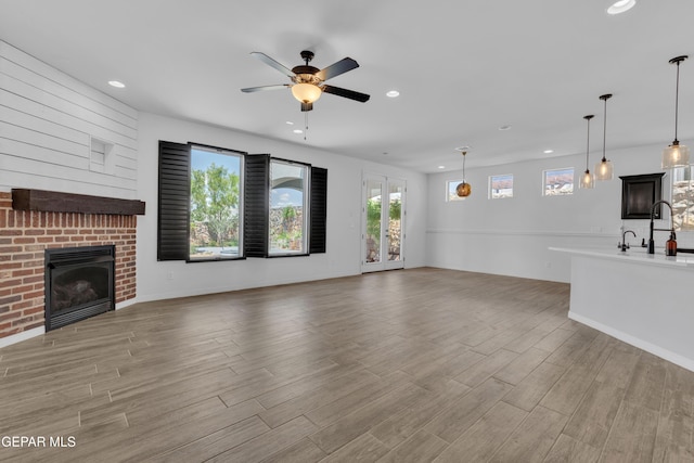 unfurnished living room featuring a fireplace, recessed lighting, a ceiling fan, light wood-type flooring, and a sink